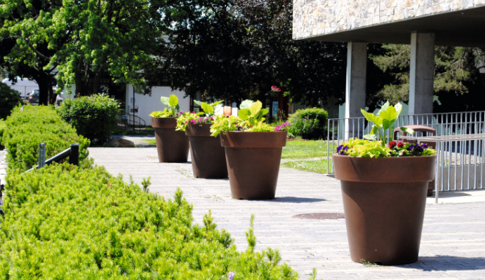 quatre pots de fleurs atech jardin modèle extravase de couleur marron sur une esplanade minérale, de la verdure à gauche