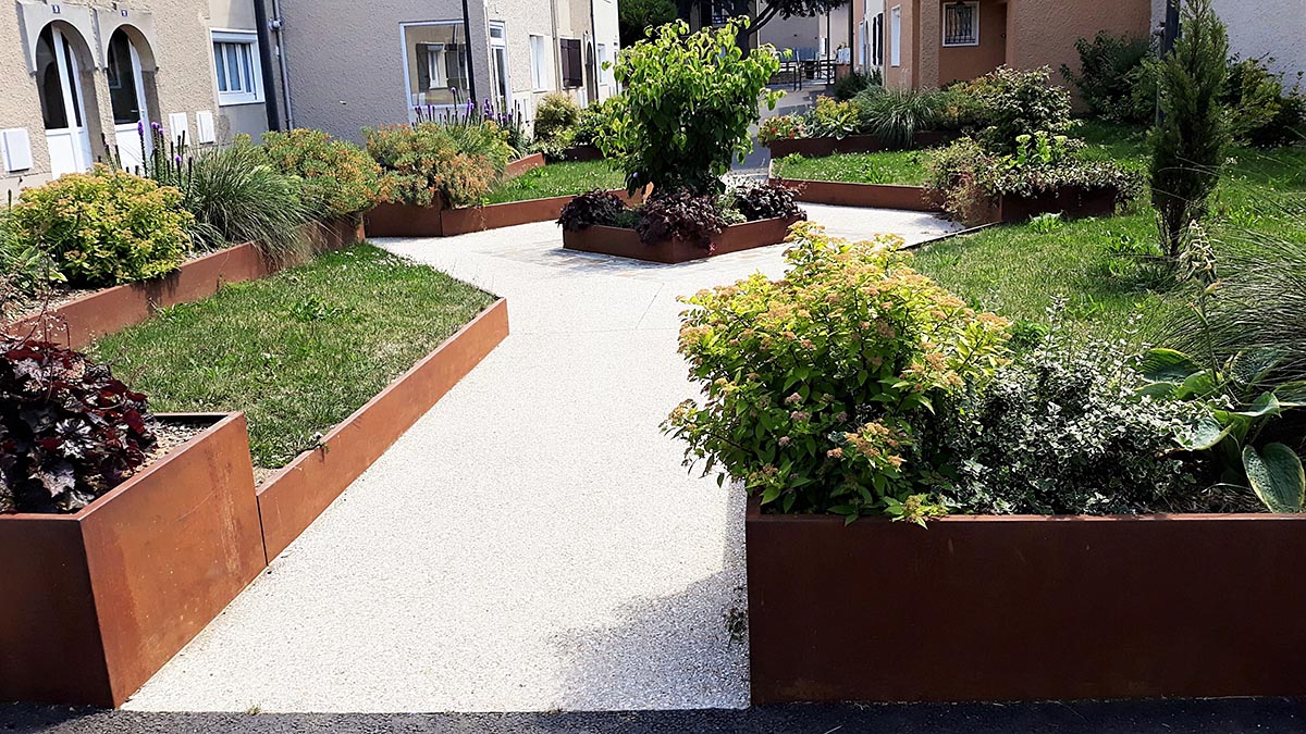 Jardin avec une allée centrale de couleur claire délimitée de chaque côté par des bordures en acier corten et un arbre au fond de l'image