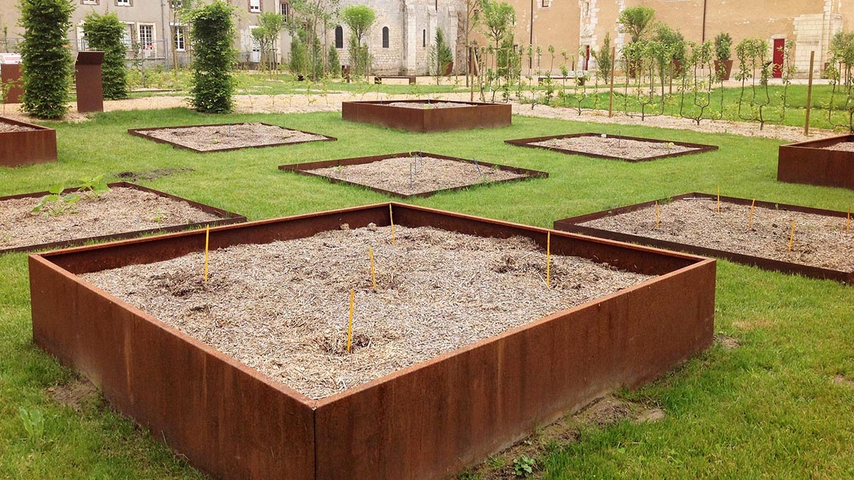 Photo montrant un bac de jardin en acier corten de couleur rouille au milieu du jardin verdoyant d'un château