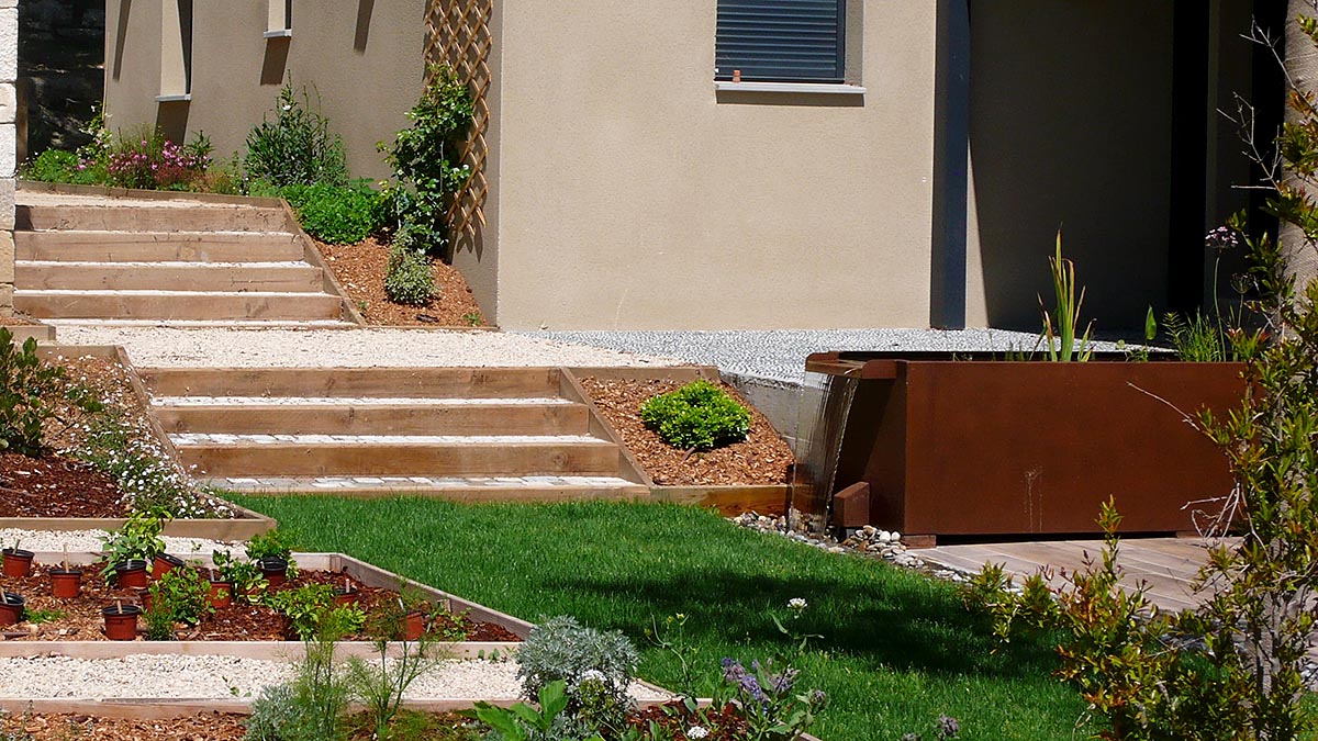 une fontaine de jardin ou table d'eau à doroite, un escalier au milieu, de la pelouse au 1er plan