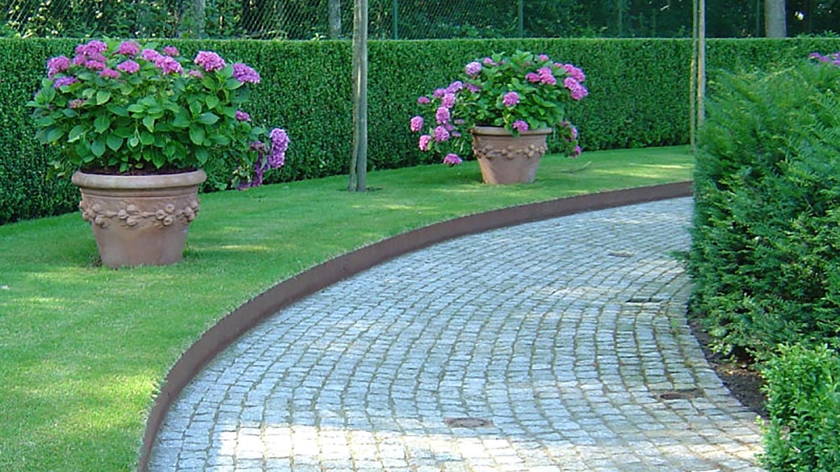 Bordure de jardin en acier corten séparant une allée pavée et une zone gazonnée