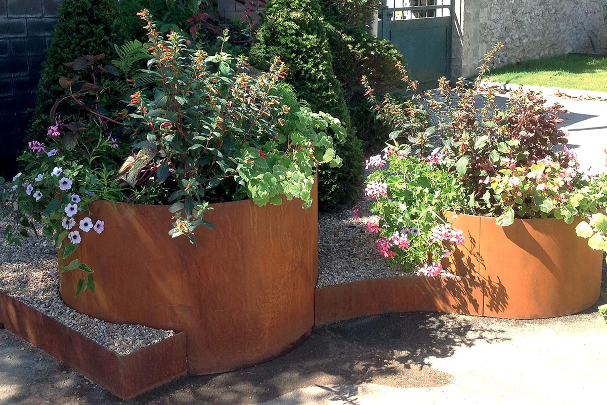 deux bacs de jardin rond en acier corten avec des végétaux et des fleurs